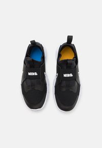 Zapatillas negras sin cordones con parte superior de malla texturada, suela blanca y logo de Nike en blanco. El interior presenta plantillas acolchadas en azul y amarillo.