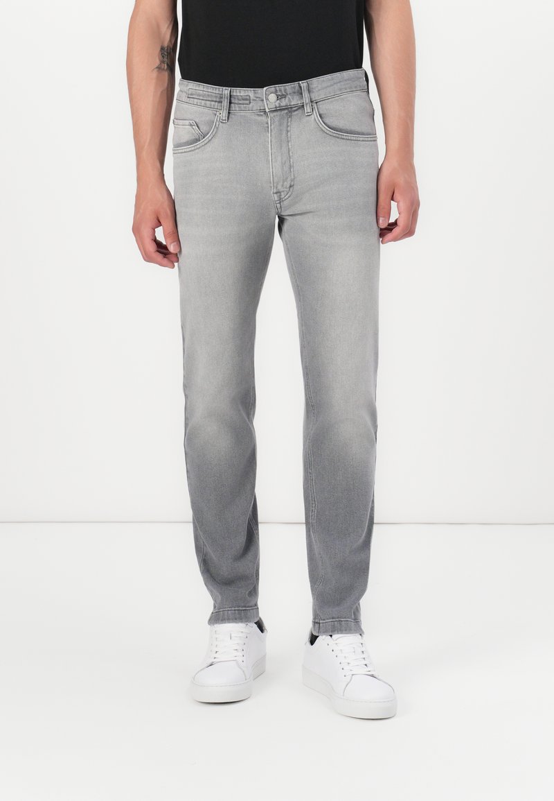 Grå denimjeans med rett ben, fem-pocket design og en lett falming. Kombinert med hvite sneakers og en svart skjorte.