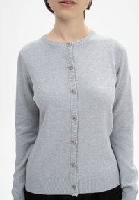 Grauer Cardigan aus weichem Strickmaterial, mit Rundhalsausschnitt, Knopfleiste und gerippten Bündchen und Saum. Subtile Textur sichtbar.