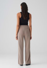 Beige wijde pantalon met zakken en een elastische tailleband, in combinatie met een aansluitend zwart tanktop. Soepele textuur en een ontspannen pasvorm.