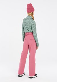 Camicia verde a maniche lunghe con pois neri, abbinata a pantaloni rosa a vita alta e stivaletti neri da neve; berretto lavorato a maglia rosa caldo.
