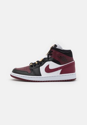 Zapatilla alta en negro, blanco y rojo oscuro con el logo de Nike, cordones negros y detalles dorados en los cordones, sobre un fondo blanco liso.