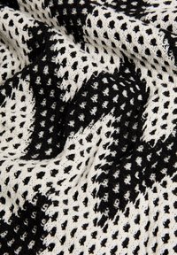 Tessuto lavorato a maglia in bianco e nero con un motivo aperto e testurizzato caratterizzato da piccole forme a diamante. Il materiale sembra morbido e leggero.