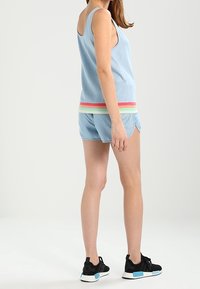 Canottiera di cotone blu con una cintura multicolore a strisce, abbinata a pantaloni corti blu. Scarpe da ginnastica nere con dettagli blu.