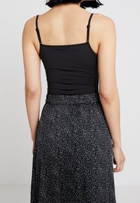 Černý přiléhavý top bez rukávů s tenkými nastavovacími ramínky, v kombinaci s dlouhou černou sukní s jemným bílým tečkovaným vzorem.