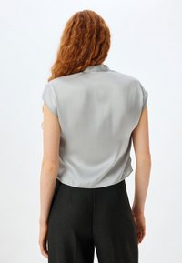 Hopeat silkki lyhythihainen crop-top, jossa on kauluskanta. Sileä pinta, minimaalinen muotoilu ja tasainen väri ilman näkyviä kuvioita.