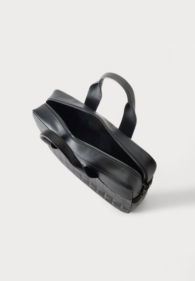Porte-documents en cuir noir avec fermeture éclair ouverte sur le dessus, poignées rembourrées et surface avant texturée sur un fond clair uni.