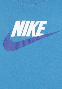 Modrá bavlněná tričko s kulatým výstřihem, s velkým bílým logem "NIKE" a fialovým designem swoosh pod ním.