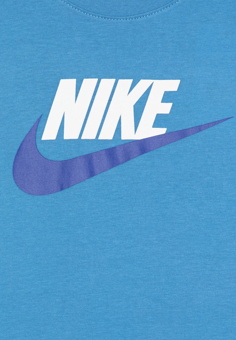 Niebieska bawełniana koszulka z okrągłym dekoltem, z dużym białym logo "NIKE" i fioletowym wzorem "swoosh" poniżej.