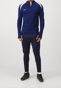 Nike blue training top with hexagonal texture and white shoulder accents, paired with navy athletic pants and black cleats.