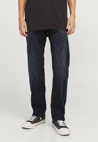 Jeans de mezclilla azul oscuro con un corte recto, combinados con zapatillas negras con cordones blancos y suelas de goma. Diseño sencillo y limpio.