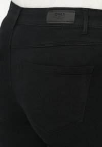 Zwarte denim broek met een slim fit, voorzien van een achterzak en gestikte details. Het label op de tailleband leest "ONLY" met een logo.
