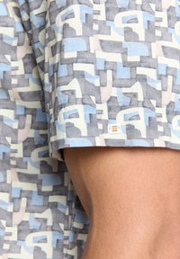 Korte mouwen overhemd met een geometrisch patroon in lichtblauw, grijs en beige. Gemaakt van stof met een gladde textuur; heeft een label op de zoom.