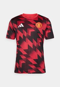 Rotes und schwarzes Manchester United-Trikot mit einem geometrischen Muster, kurzen Ärmeln, Rundhalsausschnitt und gesticktem Vereinslogo auf der Brust.