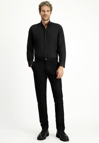 Zwarte overhemd met knopen en lange mouwen, gecombineerd met zwarte broek en zwarte schoenen. De stof lijkt glad en heeft een op maat gemaakte pasvorm.