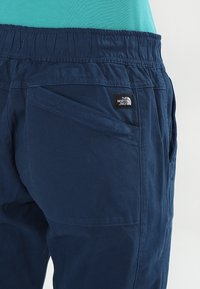 Pantaloni blu navy con elastico in vita, dotati di tasche laterali, un tessuto resistente e una patch logo nera sul retro.