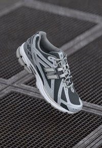 Gray athletic shoe with mesh and synthetic upper, featuring reflective accents and a cushioned sole. Intricate side design with laces.