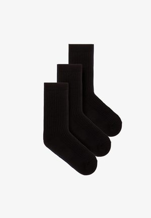 Trzy pary prostych czarnych prążkowanych skarpet za kostkę ułożonych nakładających się na siebie na białym tle.