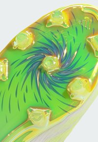 Κοντινή λήψη της σόλας αθλητικού παπουτσιού ποδοσφαίρου σε πράσινο και κίτρινο χρώμα, με διαφανή καρφιά και μαύρο στροβιλιζόμ ενο μοτίβο.