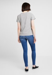 Šedé tričko s krátkým rukávem v kombinaci s modrými slim fit džíny, které mají klasický střih, hladkou texturu a jednoduchý design. Obuv tvoří černé tenisky.