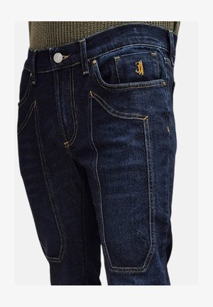 Jeans in denim blu scuro con cuciture gialle a contrasto, un bottone argentato e un design unico delle tasche. Il tessuto ha una texture liscia e una vestibilità strutturata.