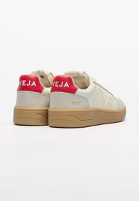 Beige and gray sneakers with red heel accents. Features a textured suede finish and subtle branding. Rubber sole with a gum color.