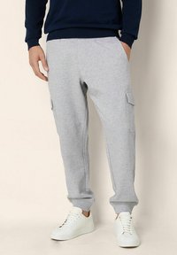 Grå sweatpants i mjuk tyg, med sidofickor, smalnande mudd och elastisk midja. Bärs med vita sneakers.
