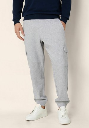 Pantalones de chándal grises fabricados con tejido suave, con bolsillos laterales de carga, puños ajustados y una cintura elástica. Llevados con zapatillas blancas.