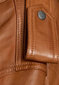 Braune Lederhandtasche mit glatter Textur, kontrastierenden Nähten und einem Druckknopfverschluss mit metallischem Akzent. Langlebiges und kompaktes Design.
