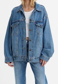 Ljusblå jeansjacka i oversize-stil med knäppningar, två bröstfickor och en något fransad fåll, matchad med tillhörande jeans.