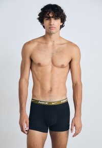 Boxers negros de Nike con una cinturilla elástica dorada que presenta el logo de la marca. Tejido suave, diseño ajustado y longitud hasta mitad del muslo.
