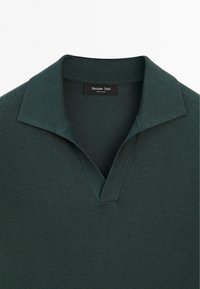 Tmavě zelená pletená polo košile s otevřeným límcem ve tvaru V, zdobená detailem šití a s etiketou "Massimo Dutti" uvnitř límce.