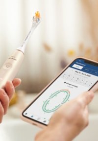 Brosse à dents électrique avec un manche accentué en or et un head de poils multicolores, tenue à côté d'un smartphone affichant un tableau de bord dentaire.