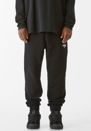 Svarta sweatpants med en avslappnad passform, elastiska muddar och en liten vit logotyp på vänster sida. Tillverkade av mjukt, texturerat tyg.