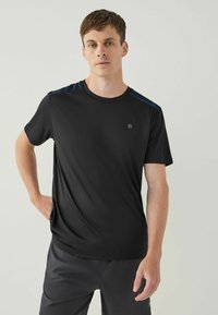 Sort atletisk t-shirt med korte ærmer, der har mørkeblå skulderdetaljer og et lille logo på brystet. Glat, let vævning.