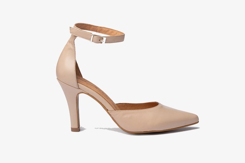 Zapato de tacón alto de cuero nude con punta afilada y tira en el tobillo. Presenta una textura suave y un tacón delgado y cónico.