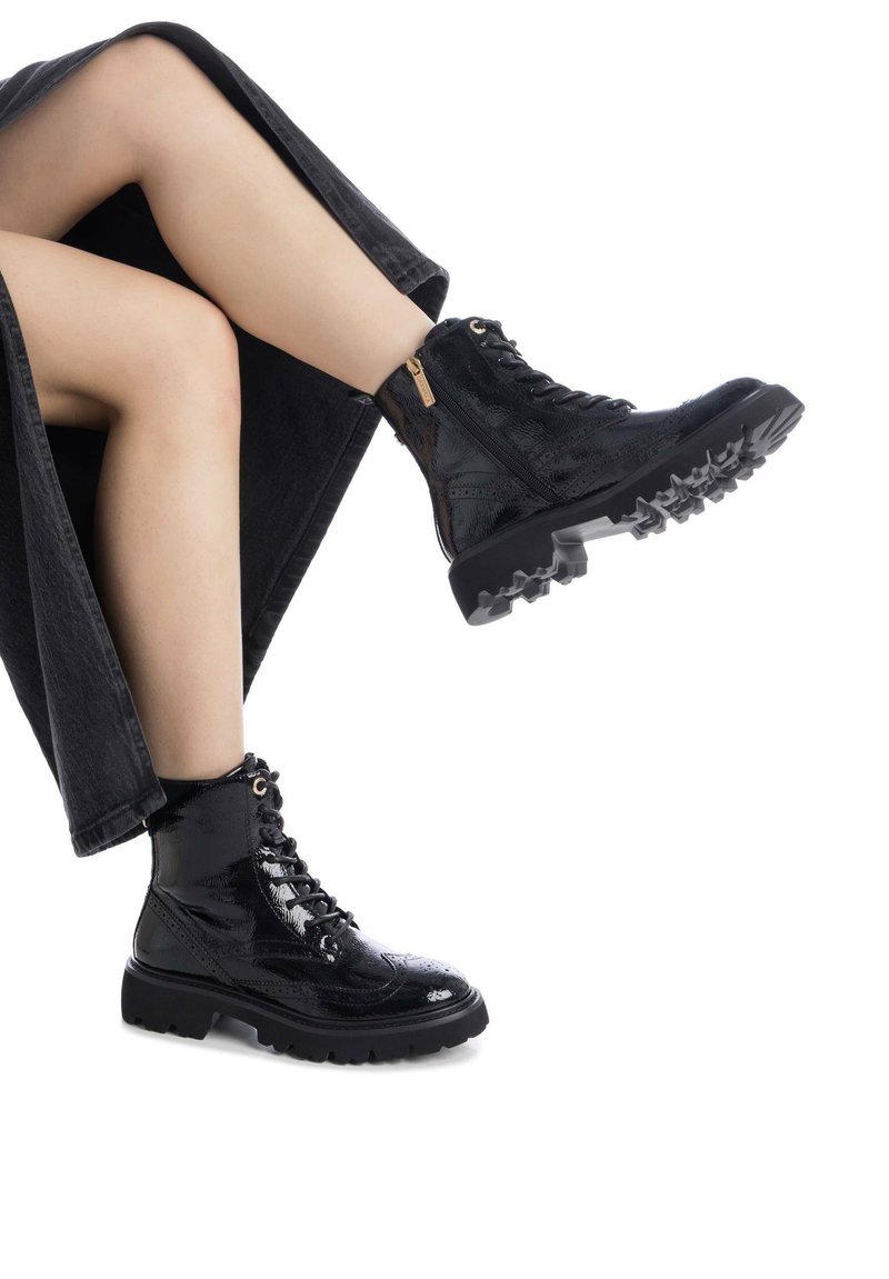 Botines de charol negro con parte superior texturizada, suela de goma con tacos, punta redonda y acentos de hardware en tono dorado. Cierre de cordones ajustado.