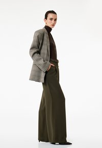 Grå ternet blazer, brun turtleneck og olivengrønne vide bukser. Glatte stoffer, afslappet pasform, med et bælte og spidse sorte sko.