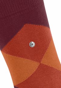 Calzino colorato con un motivo geometrico di sezioni viola, arancione e ruggine, caratterizzato da un piccolo marchio d'argento cucito sul tessuto.