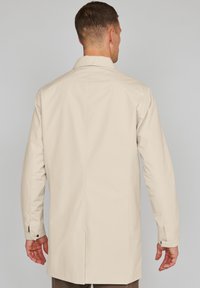 Abrigo impermeable beige con un diseño recto y un gran cuello. Presenta mangas largas, puños abotonados y aberturas de ventilación en la parte posterior.