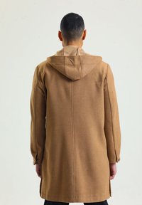 Brauner, kapuzenloser Mantel mit geradem Schnitt und langen Ärmeln. Verfügt über einen strukturierten Stoff und seitliche Schlitze für Bewegungsfreiheit.