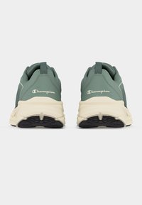 Ζεύγος πράσινων και μπεζ παπουτσιών Champion, εμφανιζόμενα από πίσω, με μαύρες υφασμάτινες σόλες και λουράκια για κράτημα στις φτέρνες.