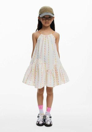 Hele värvusega kleit mitmevärviliste dekoratiivsete täppidega, volditud äärega ja spageti rihmadega. Koos mütsi ja läikivate sandaalidega.