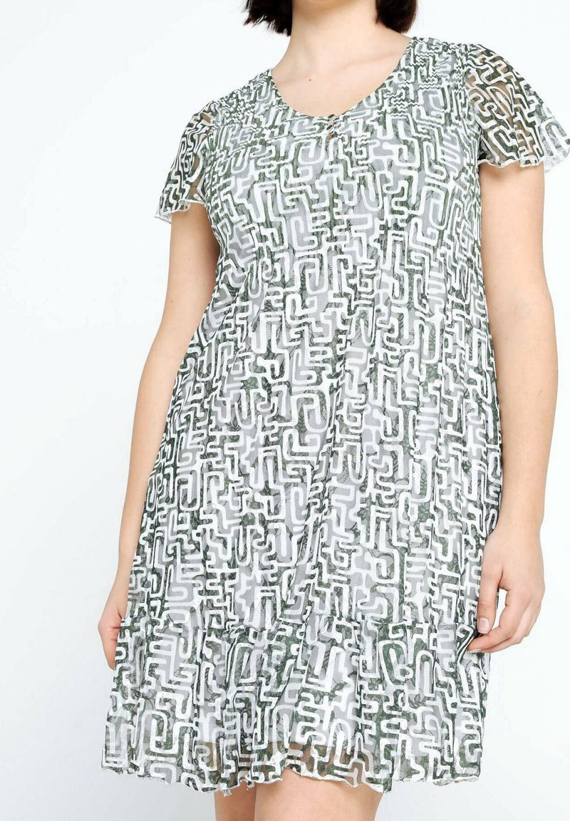 Femme portant une robe à manches courtes avec un ourlet volanté, présentant un motif géométrique abstrait noir et blanc sur un tissu transparent.