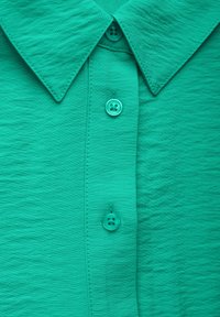 Zielona koszula z krótkim rękawem, wykonana z teksturowanej tkaniny, z klasycznym kołnierzykiem i trzema dopasowanymi guzikami na zapięciu z przodu.