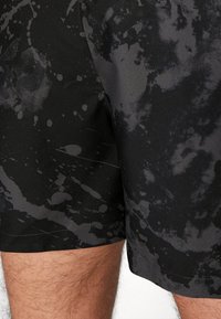 Shorts noirs avec motif abstrait éclaboussé gris portés par une personne, montrant l'ourlet et le haut des jambes.