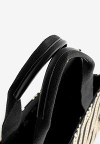 Fekete vászontáska mintás díszítésekkel, két fekete, sima tapintású fogantyúval, közeli kép a felső nyílásról és a pánt részletről.