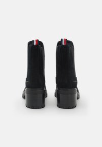 Bottines en suede noir avec un talon épais noir, présentant des accents rayés rouges et blancs à l'arrière pour un détail supplémentaire.