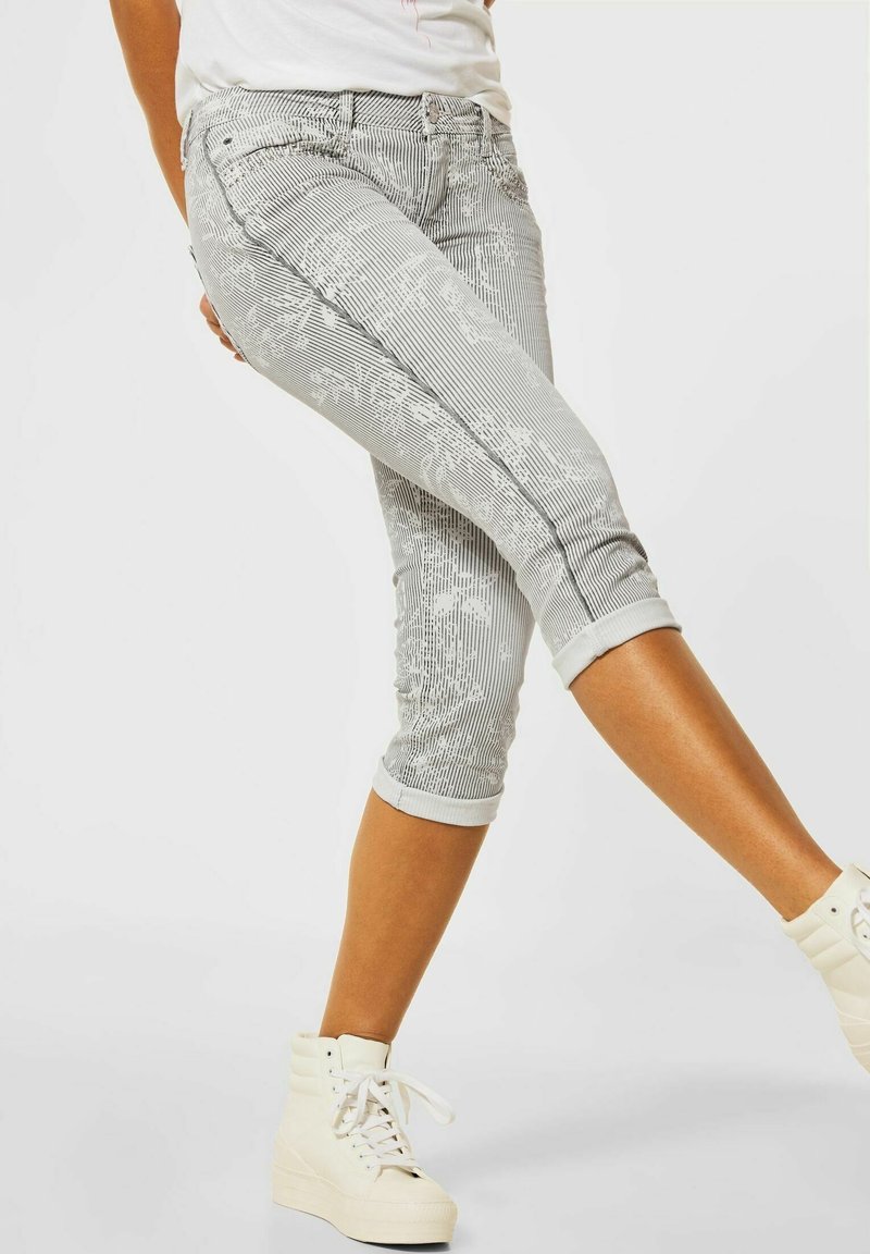 Grau Capri-Jeans mit subtilen Streifenmuster, Blumendetails, umgeschlagenen Säumen und Fronttaschen, kombiniert mit weißen High-Top-Sneakern.