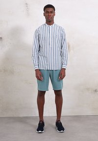Striped long-sleeve shirt in light blue and white, paired with mint green shorts. Worn with black athletic shoes featuring red accents.